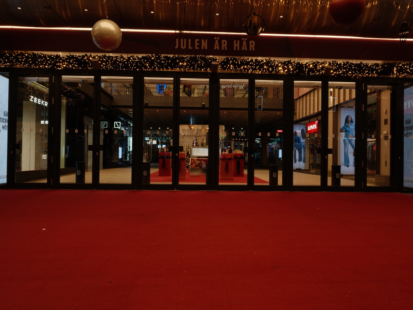 Shopping mall entrance at Christmas. A massive red carpet covers the entire flat approach to wide glass doors under Christmas lights.