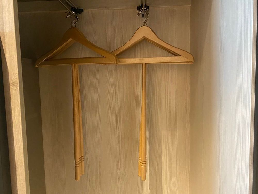 Two wooden hangers in a wardrobe, each fitted with a long wooden rod hanging down so the hanger can be reached and lifted from below.